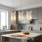 Full view of three modern chrome crystal pendant lights installed above a contemporary kitchen island with ambient lighting and natural daylight.