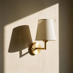 Close-up of a fabric wall sconce with a brushed metal arm mounted on a textured plaster wall.